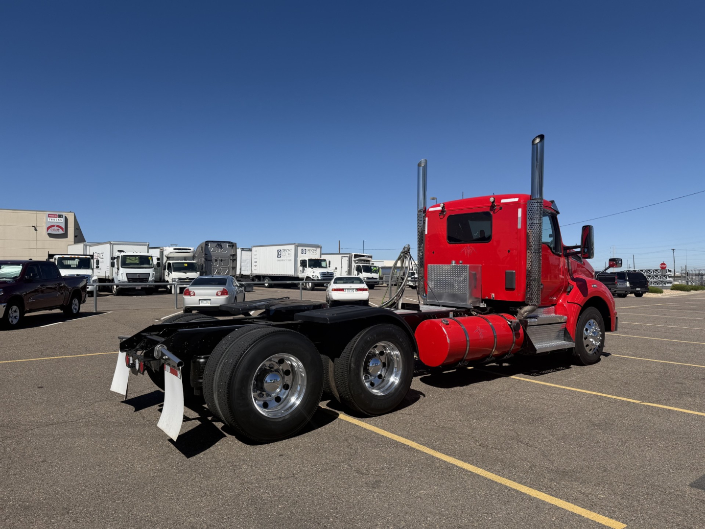 Kenworth T880 conventional daycab truck with red cab and dual rear axles, viewed from left rear, in a dealership lot.
