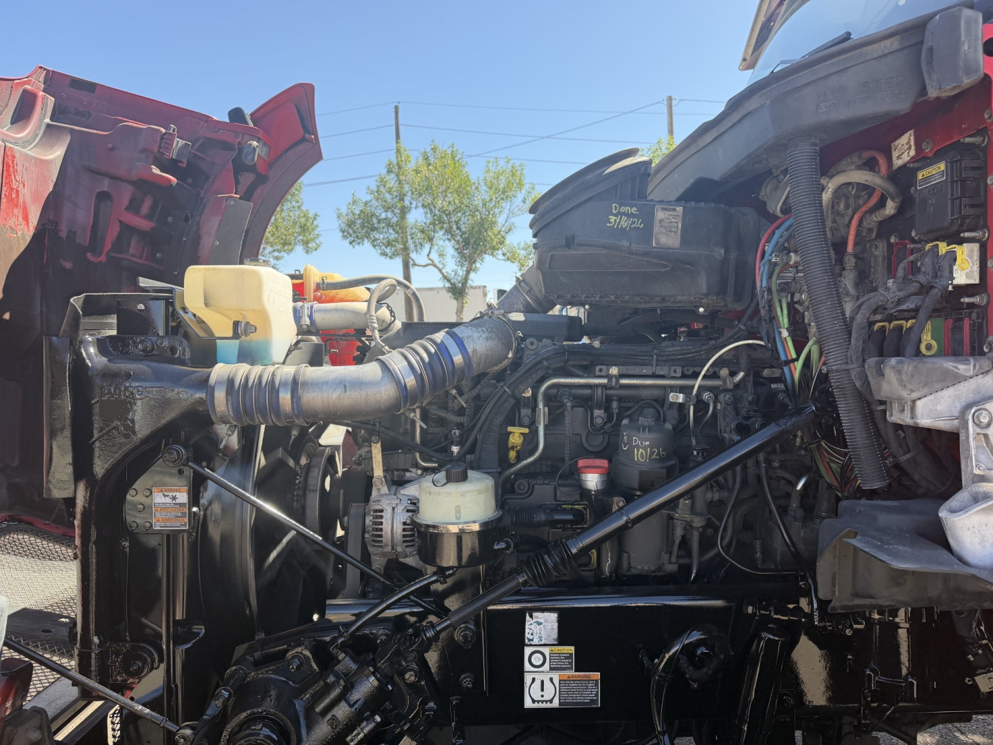 Kenworth T880 engine bay showing air intake, coolant reservoir, and various hoses and wiring.