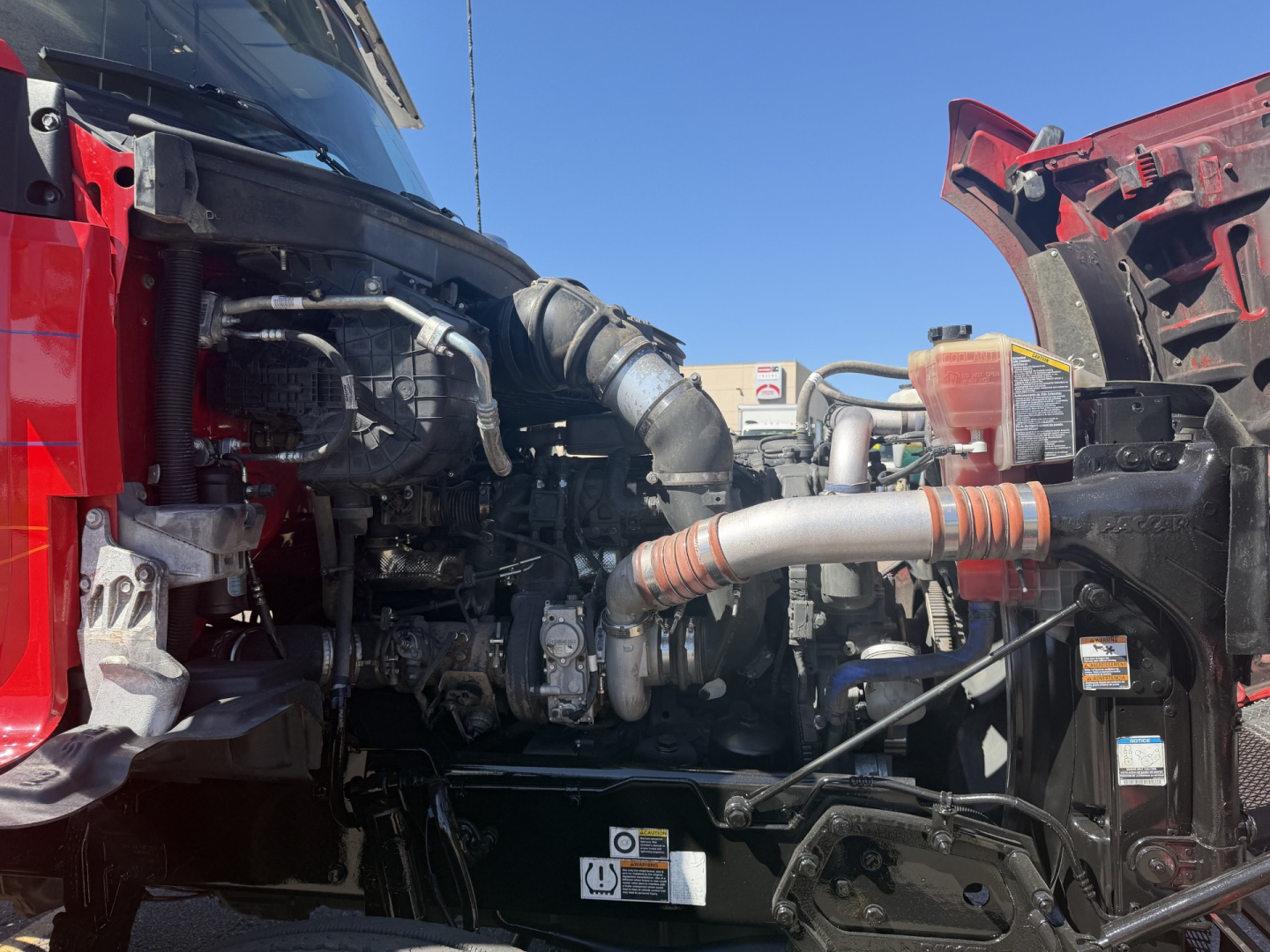 Kenworth T880 engine bay showing complex turbocharger piping and hoses between cab and engine with red fenders partially visible.