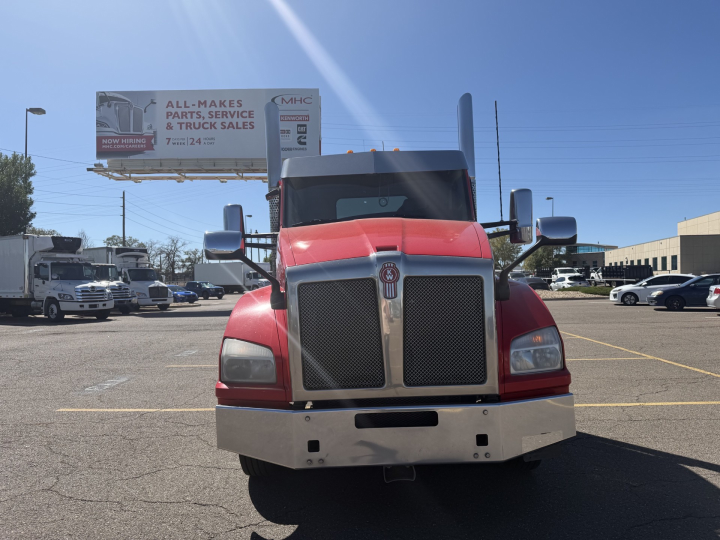 Kenworth T880 conventional daycab front view showing chrome grille, red cab, large side mirrors in a truck lot.