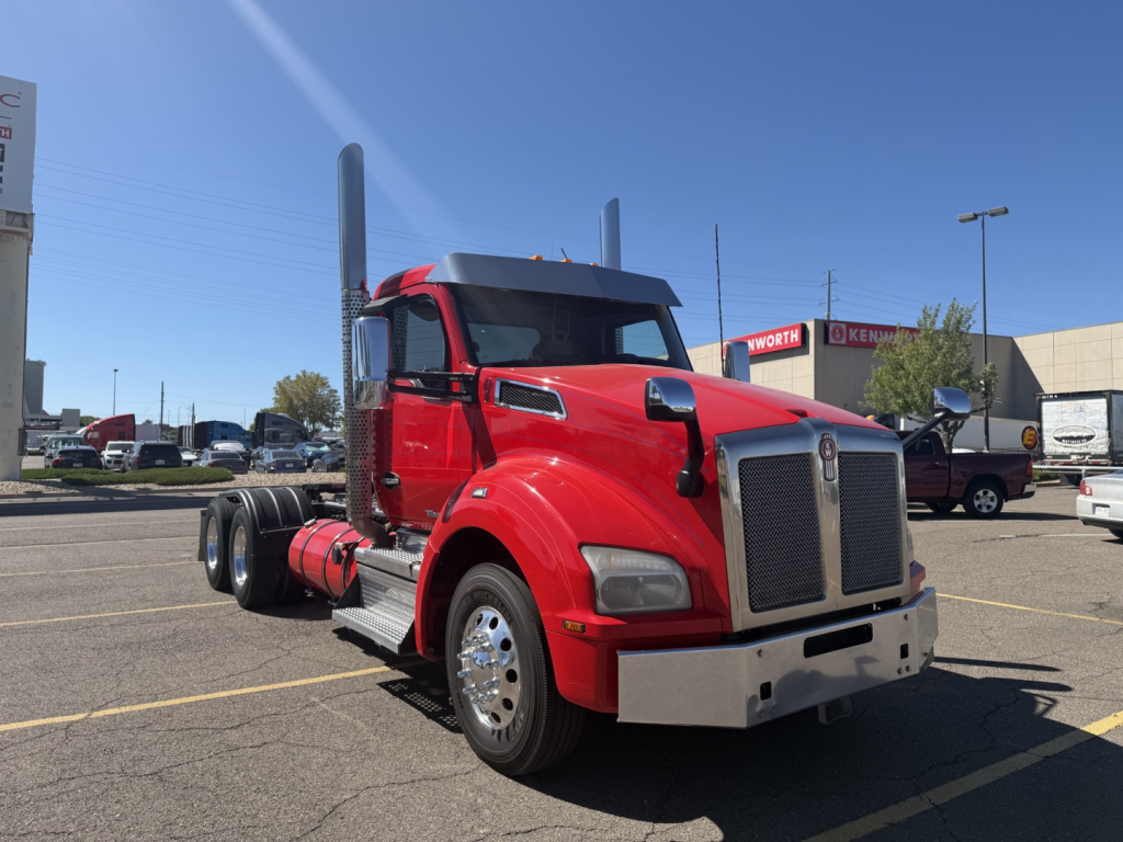Kenworth T880 conventional daycab truck in red, front-side view with tall exhaust stacks, chrome bumper, and large grille.
