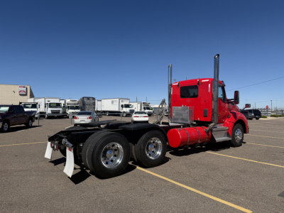Kenworth T880 conventional daycab truck with red cab and dual rear axles, viewed from left rear, in a dealership lot.