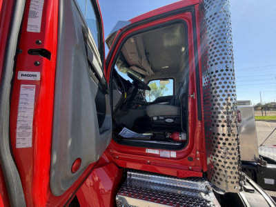 Kenworth T880 cab interior and open driver door showing red exterior, chrome exhaust stack, and steps.