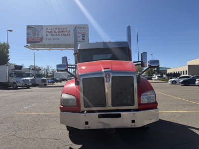 Kenworth T880 conventional daycab front view showing chrome grille, red cab, large side mirrors in a truck lot.