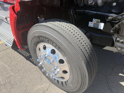 Kenworth T880 front wheel area showing Michelin tire and polished chrome hubcap under open engine bay with red fender and steps