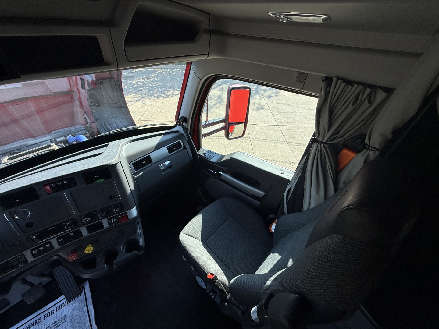 Kenworth T680 truck cab interior view showing dashboard, steering wheel, and passenger seat with window and curtain in the sleeper area.