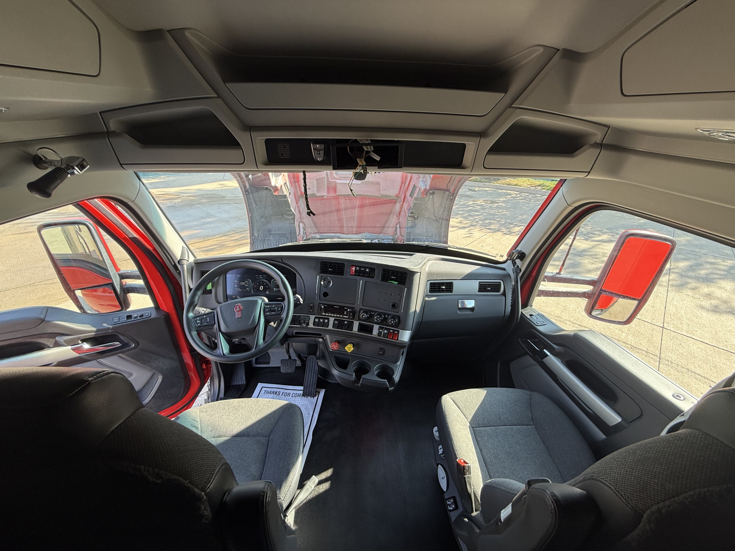 Kenworth T680 truck cockpit interior with steering wheel, dashboard screens, and two front seats visible.