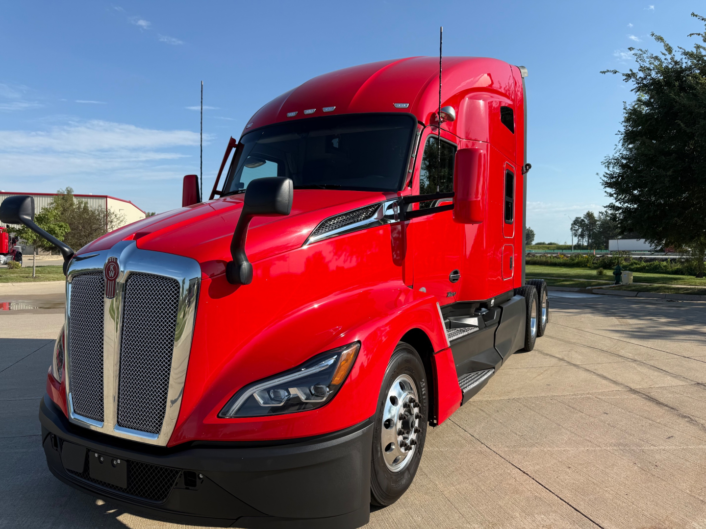 Kenworth T680 Class 8 truck in red exterior, front three-quarter view showing large chrome grille, angled daytime running lamps, sleeper-cab with side window, black bumper and wheel fenders.