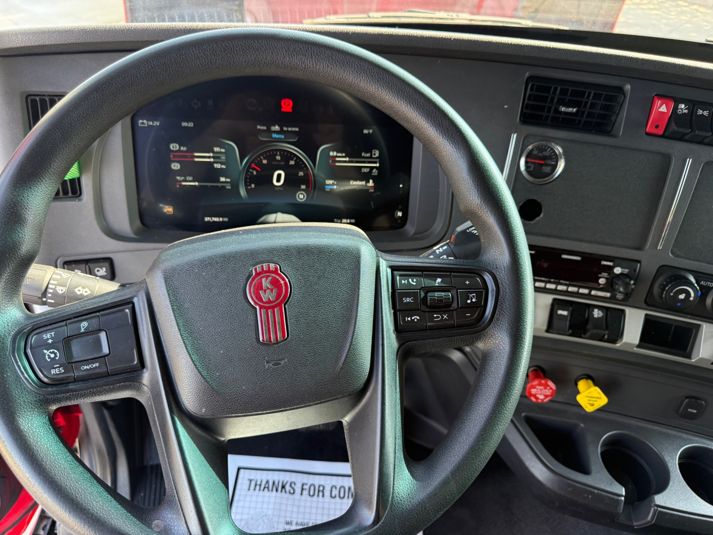 Kenworth T680 interior driver area showing steering wheel with Kenworth logo, digital gauge cluster, dashboard controls, and gear shifter area.