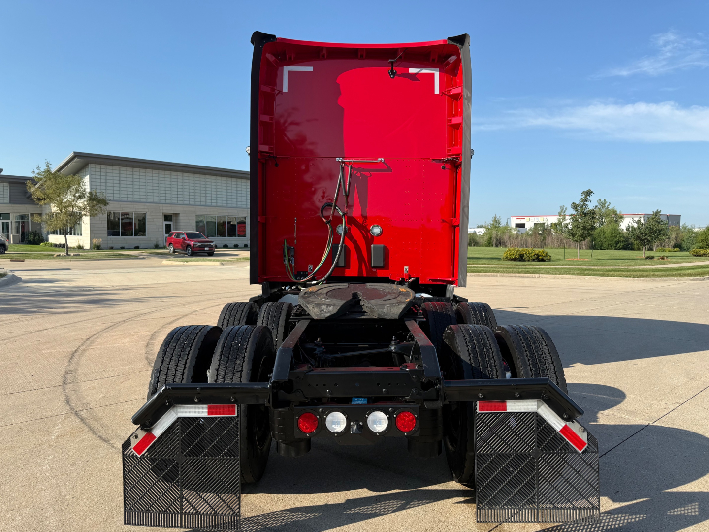 Truck rear view showing fifth wheel area and rear mud flaps of a red Kenworth T680 sleeper with dual rear axles and wheel guards.