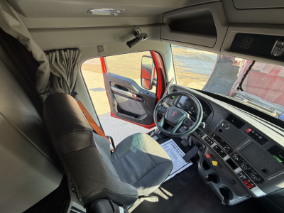 Kenworth T680 cab interior with steering wheel, dashboard, and driver's seat visible through open door; windshield and side window show exterior environment.