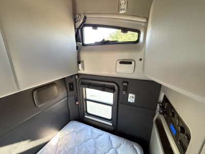 Kenworth truck cab interior showing sleeper area with window, door, and control panel; no readable labels or serial numbers visible on interior surfaces.
