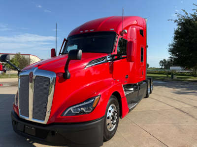 Kenworth T680 Class 8 truck in red exterior, front three-quarter view showing large chrome grille, angled daytime running lamps, sleeper-cab with side window, black bumper and wheel fenders.