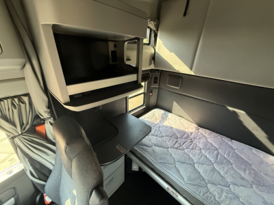 Kenworth T680 sleeper cab interior with bunk bed, captain chair, and overhead compartments; built-in microwave shelf visible.