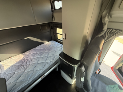 Kenworth T680 interior cabin with sleeper bunk and driver's seat; visible storage cabinet and window, with quilted mattress cover in bunk area.