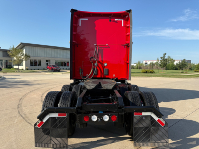 Truck rear view showing fifth wheel area and rear mud flaps of a red Kenworth T680 sleeper with dual rear axles and wheel guards.
