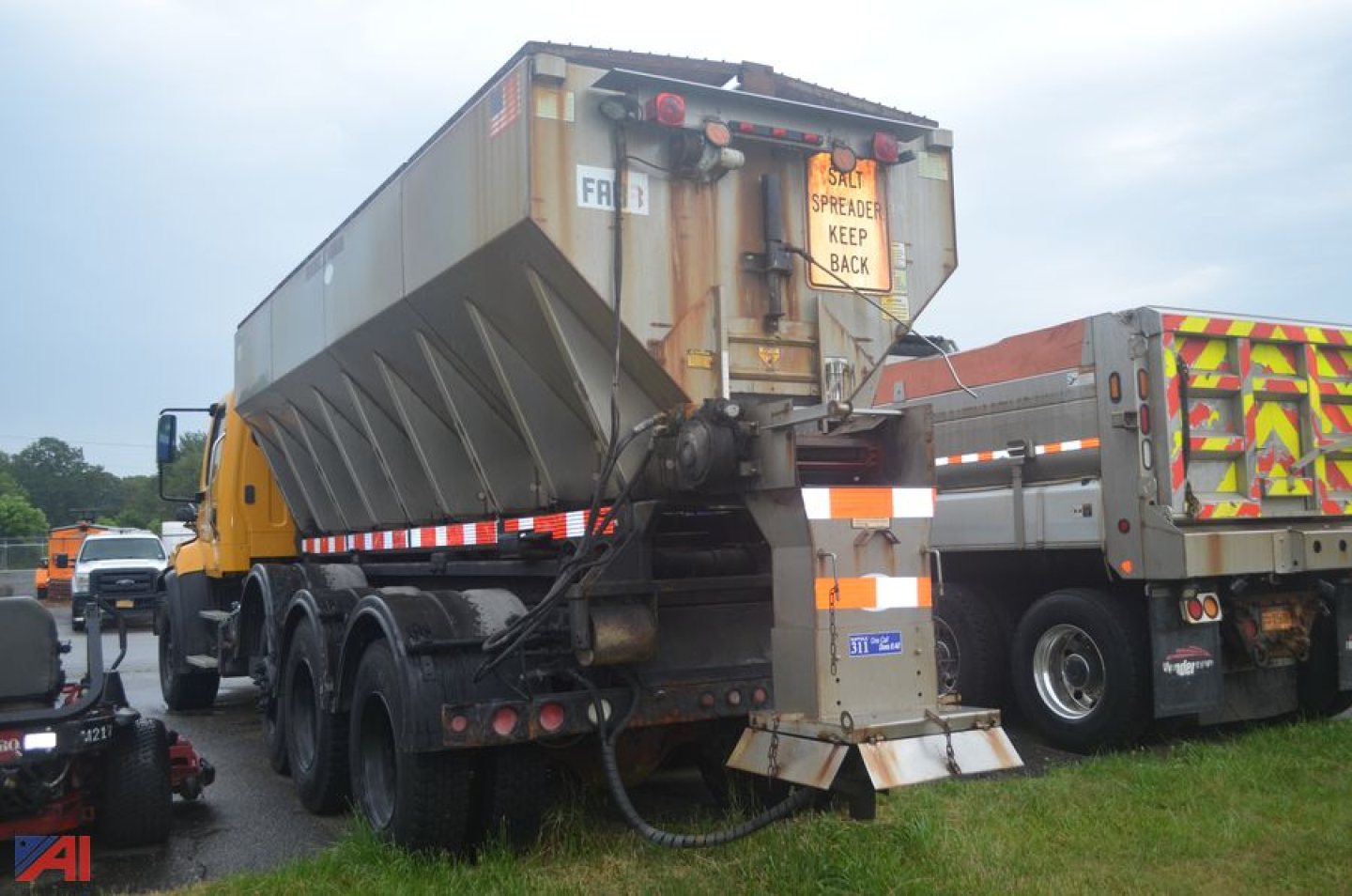 Truck rear view showing a Freightliner 114 SD sander body with spreader and multiple rear tires; caution signs and equipment attached.