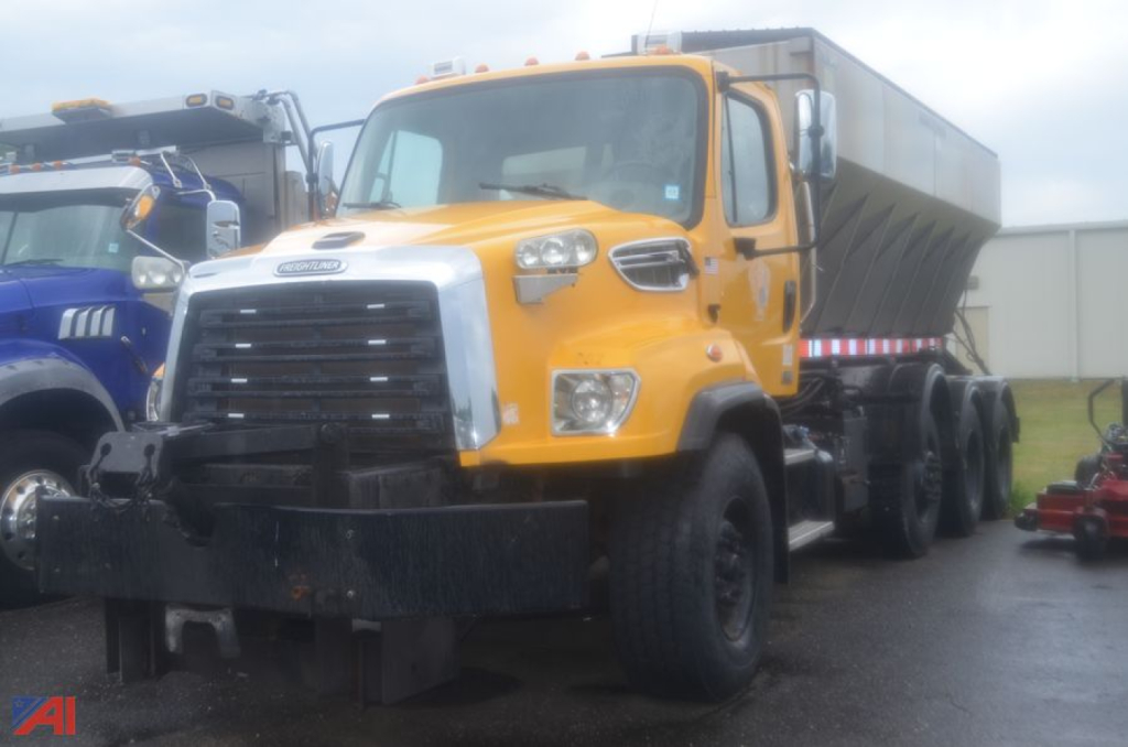 Truck cab and dump bed of a 2015 Freightliner 114 SD sander truck, yellow cab with chrome grille, black bumper, multiple wheels, side mirrors, and a gray dump bed.