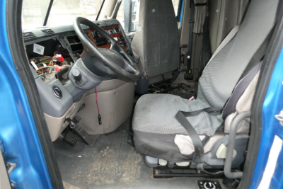 Truck cab interior showing steering wheel, dashboard with exposed wiring, driver seat with seatbelt, and dirty floor in Freightliner Cascadia cab.