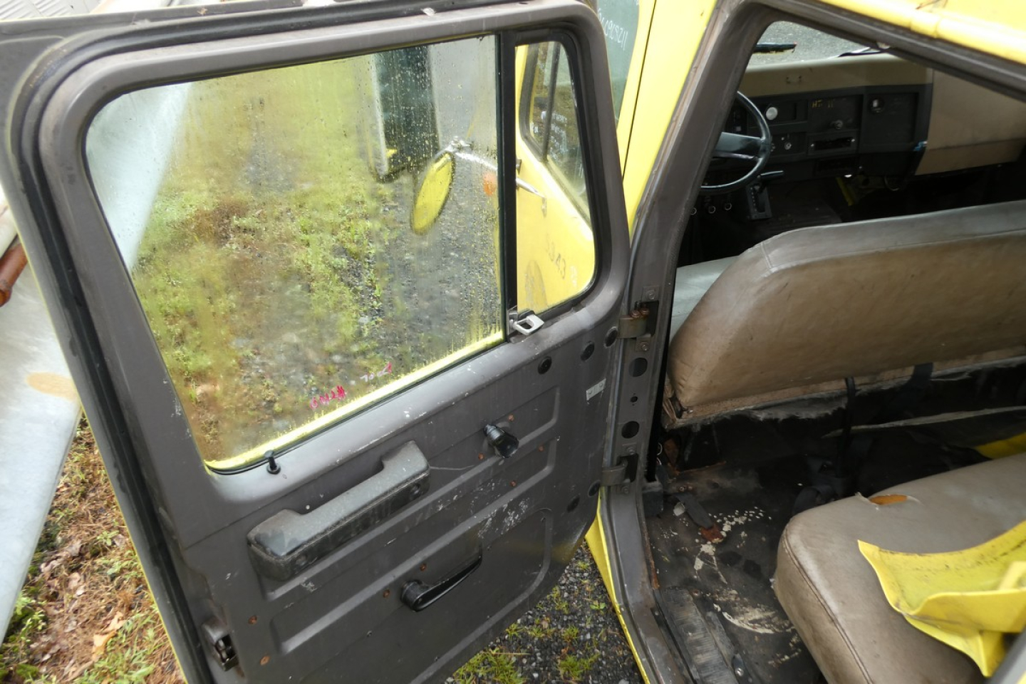 Truck cab interior and open door of an International 4700 quad cab showing worn interior, steering wheel, dashboard, beige seats, and door panel.