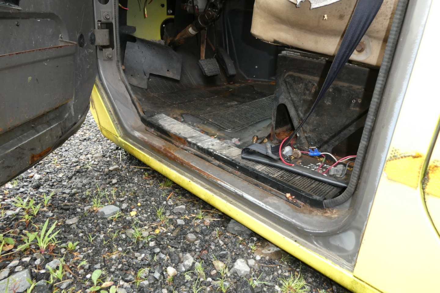 Cab interior of a used 1993 International 4700 quad cab showing open door, floor mat, exposed wiring, and yellow exterior trim at the entry threshold.