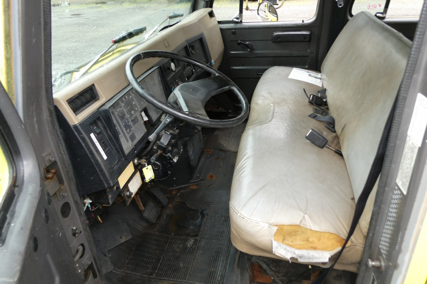 International 4700 cab interior showing steering wheel, dashboard, and bench seat with light gray upholstery.