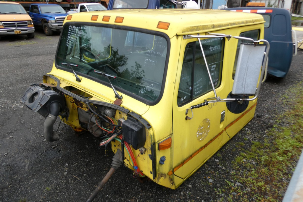 Quad cab truck cab section showing exposed wiring and drivetrain components at front, yellow paint, side window, rear view mirrors.