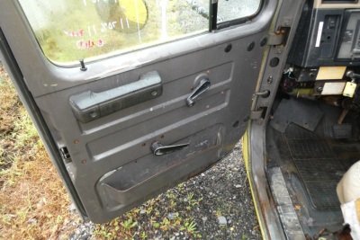 Truck cab interior door panel showing manual window crank and door handle in a used International 4700 cab; visible dashboard edge and entry area.