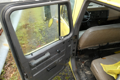Truck cab interior and open door of an International 4700 quad cab showing worn interior, steering wheel, dashboard, beige seats, and door panel.