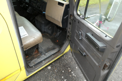 Cab interior of a yellow International 4700 with a beige seat, door open, showing the dashboard and entry step.