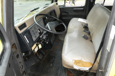 International 4700 cab interior showing steering wheel, dashboard, and bench seat with light gray upholstery.