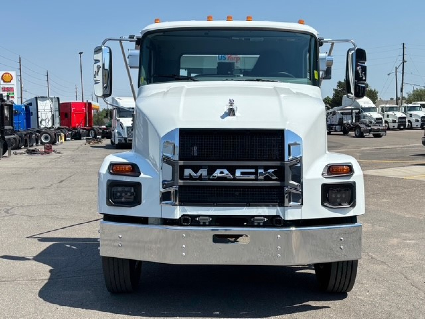Front view of a white 2026 Mack MD7 truck showing large chrome grille with MACK lettering, rectangular headlights, bumper, and hood ornament.