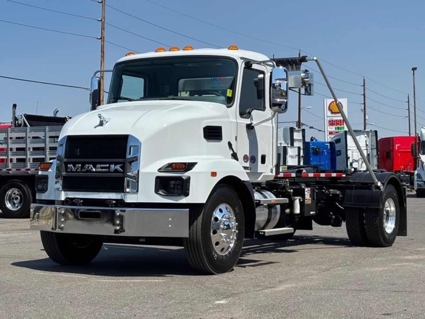 Mack MD7 hooklift truck in white, front three-quarter view showing chrome bumper, grille with MACK badge, cab with orange clearance lights, and remote hooklift chassis.