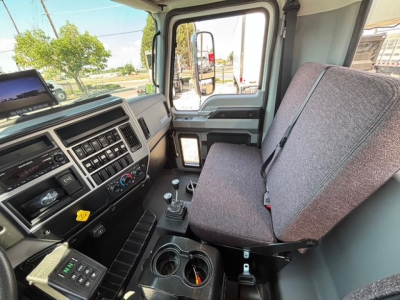 Cab interior of a new 2026 Mack MD7 hooklift truck showing driver seat, steering wheel, center console, gear shifter, and dashboard controls with window view.