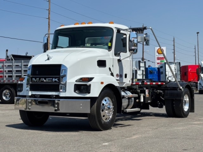 Mack MD7 hooklift truck in white, front three-quarter view showing chrome bumper, grille with MACK badge, cab with orange clearance lights, and remote hooklift chassis.