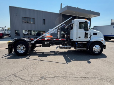 Mack MD7 hooklift truck side view showing hydraulic tilting components and cab with white exterior