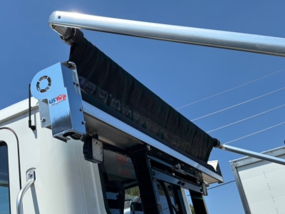 Mack MD7 hooklift truck cab corner showing UStar tarp system and hydraulic components.