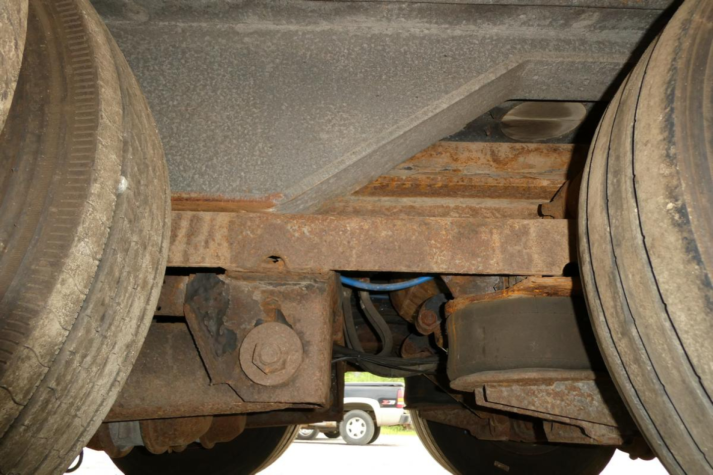Trailer underside showing axles and suspension components with rust on frame and leaf springs.