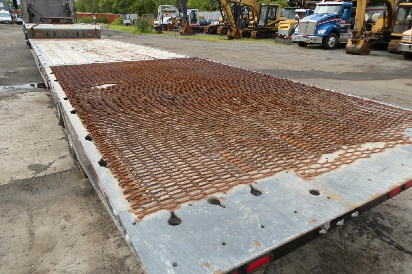 Flatbed trailer deck with rusty chain-link grid surface and metal ramp in background.