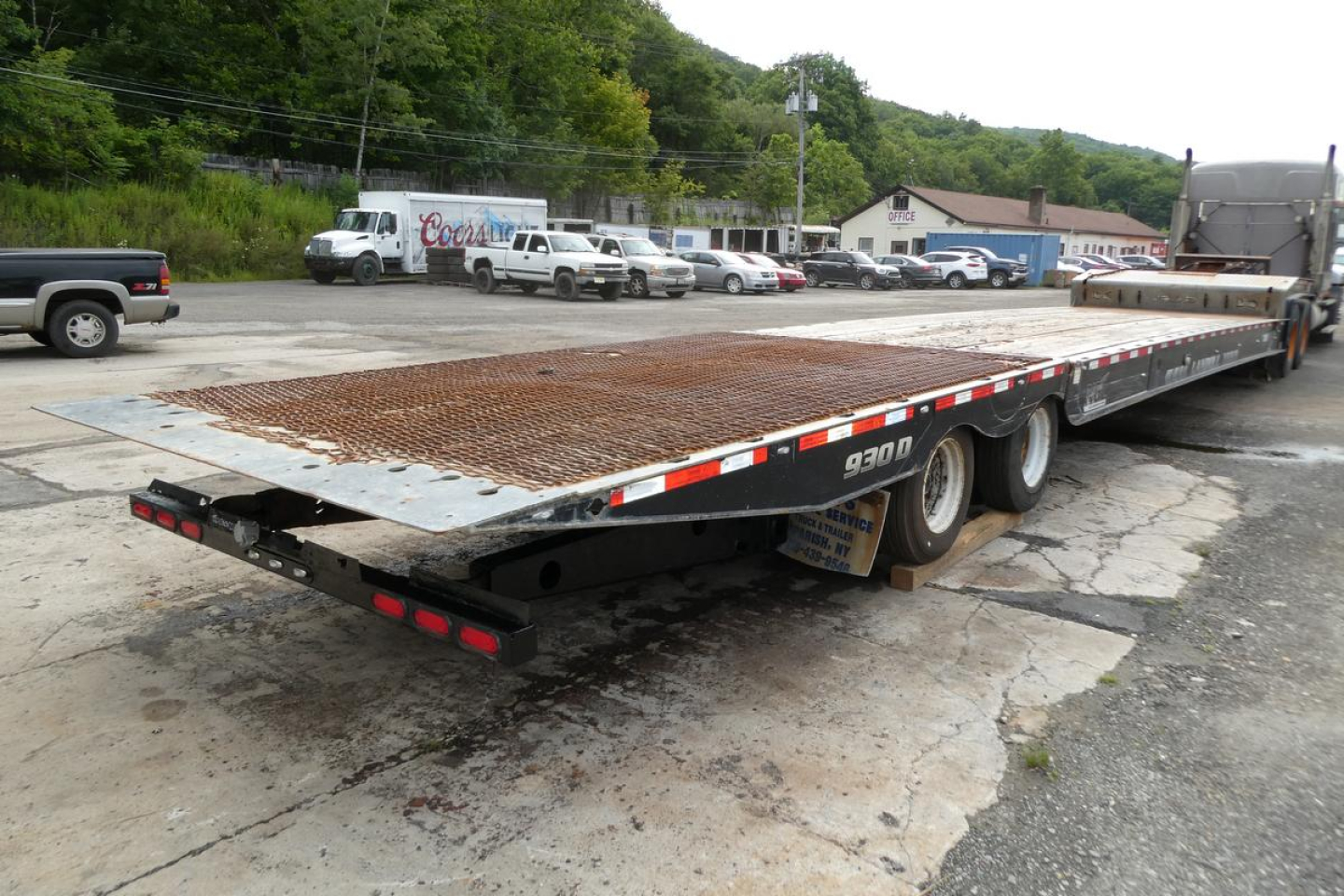 NGL flatbed trailer showing 930D model, steel grated deck, rear underride guards, and multiple axles in a used condition.