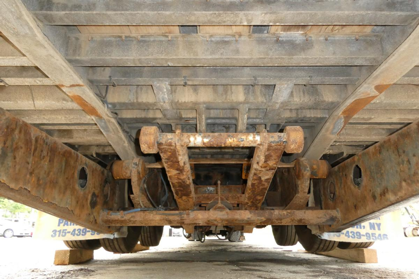 Underbelly of a trailer showing rusty chassis rails and center support beams, with wheels and underside visible.