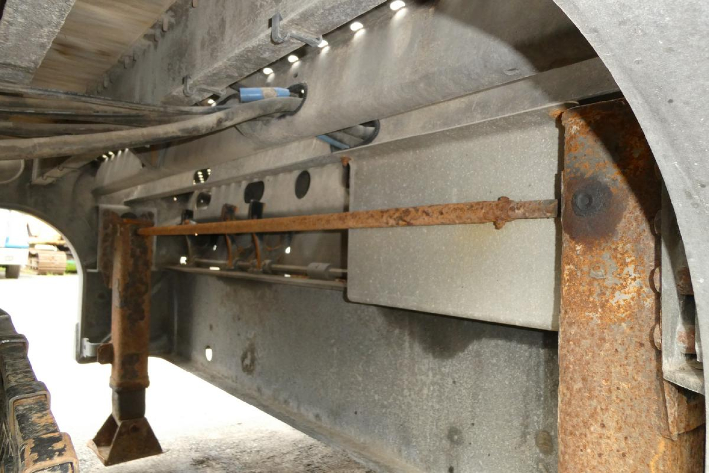 Underbelly of a Landoll 930D NGL trailer showing metal frame, rusted crossmembers, hydraulic line, and support brackets.