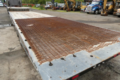 Flatbed trailer deck with rusty chain-link grid surface and metal ramp in background.