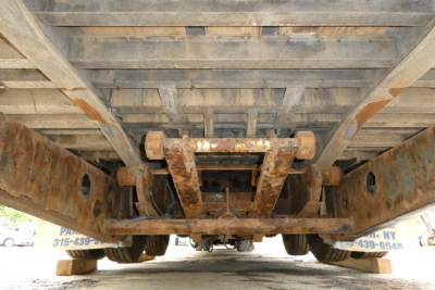 Underbelly of a trailer showing rusty chassis rails and center support beams, with wheels and underside visible.