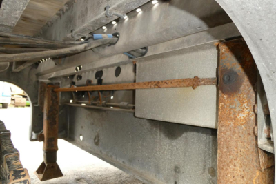 Underbelly of a Landoll 930D NGL trailer showing metal frame, rusted crossmembers, hydraulic line, and support brackets.