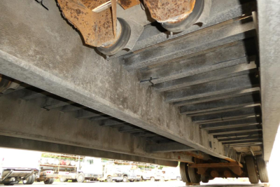 Underbelly of a Landoll trailer showing steel cross members, riveted rails, and wheel assembly with rusted pins; view from beneath the trailer.