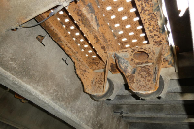 Photo of a rusty trailer undercarriage showing a forged metal frame, perforated guard, and roller wheel components on a Landoll 930D NGL trailer.