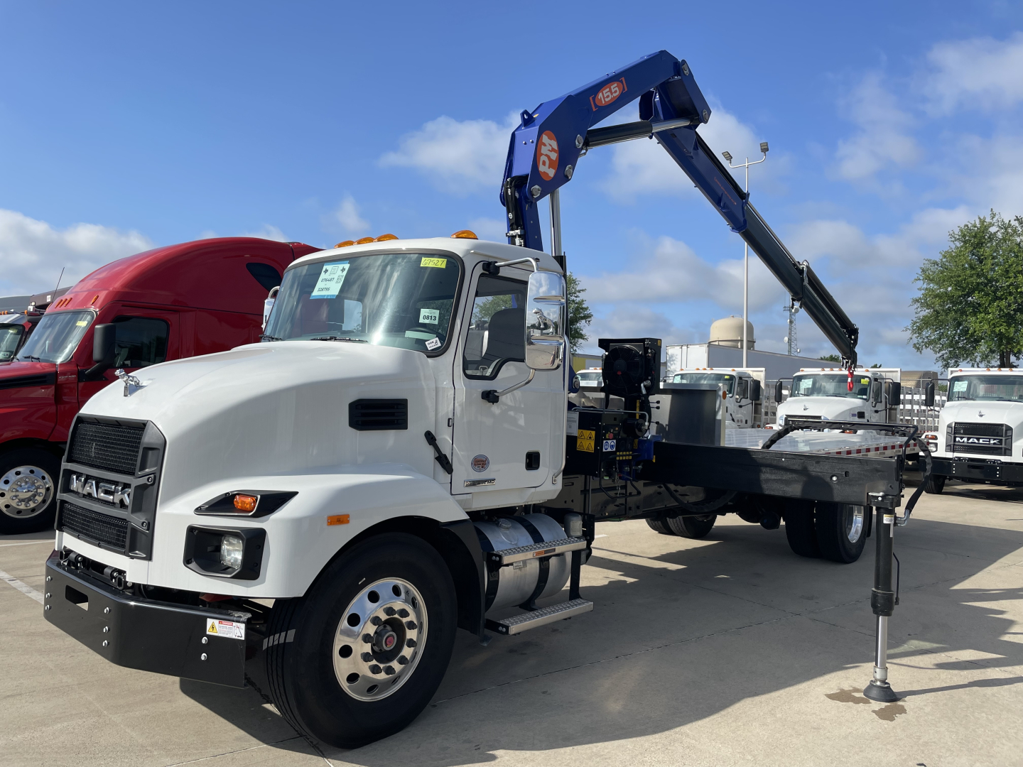 Mack MD7 boom truck showing hydraulic boom and flatbed with stabilizer leg visible.