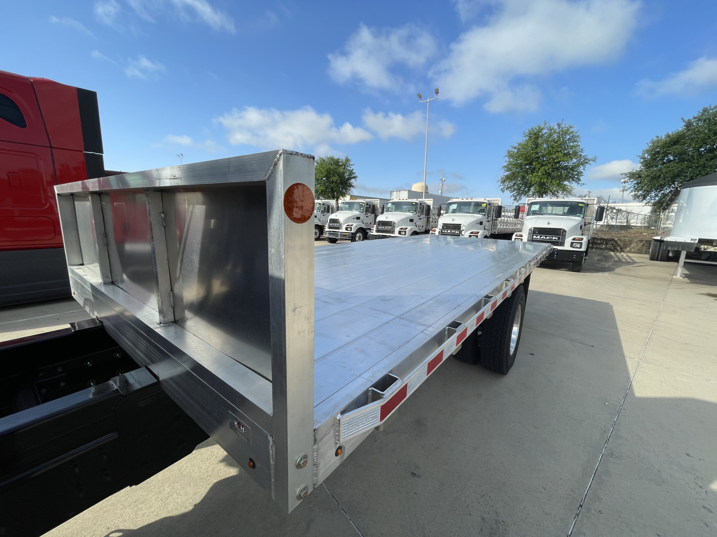 Flatbed trailer with metal side rails attached to a Mack MD7 truck chassis showing polished aluminum deck and reflective safety tape on the edge.