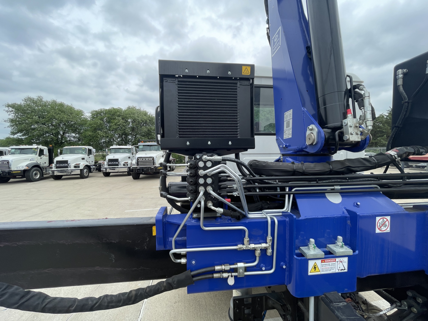 Boom truck crane on Mack MD7 showing hydraulic lines and control box with radiator-like component mounted on blue structure.